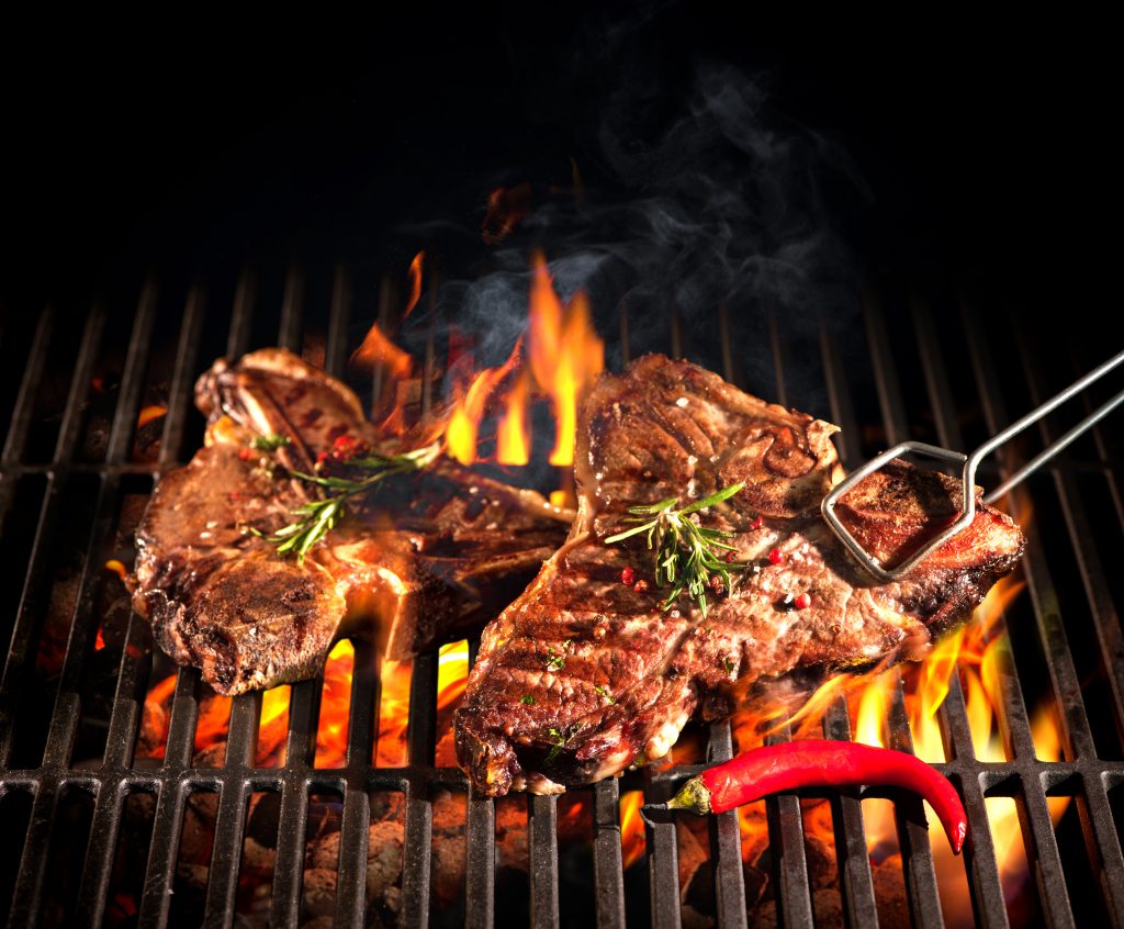 T-Bone Steak sizzling on the grill wiht a pepper 